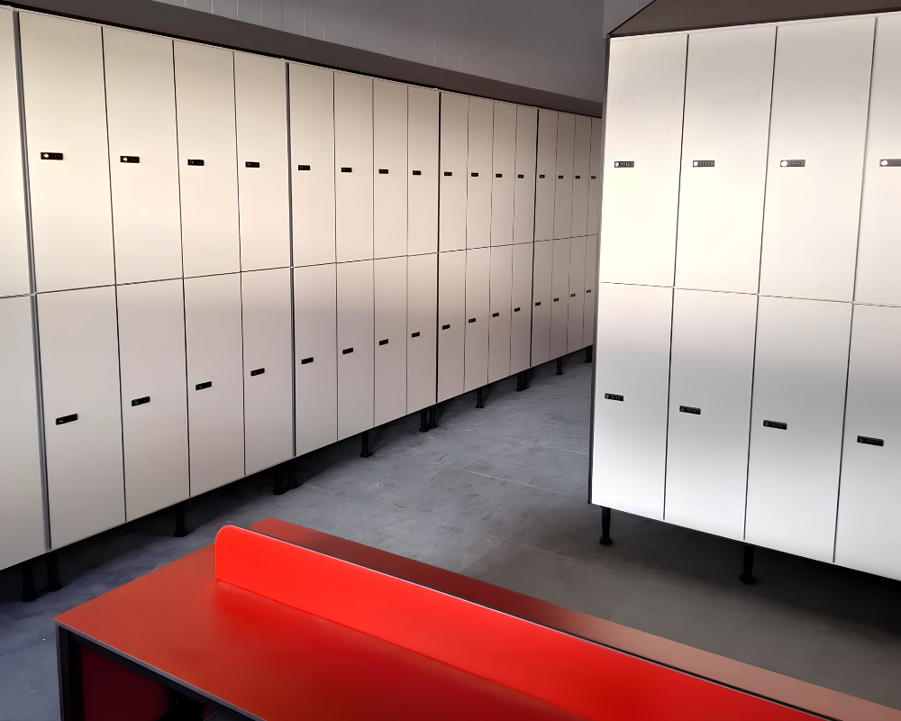 Taquillas fenólicas blancas con banco rojo Taquillas fenólicas blancas de dos puertas en L con banco rojo en un vestuario de fábrica